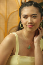 Woman wearing a yellow top with a decorative green pendant, against a warm-toned background.