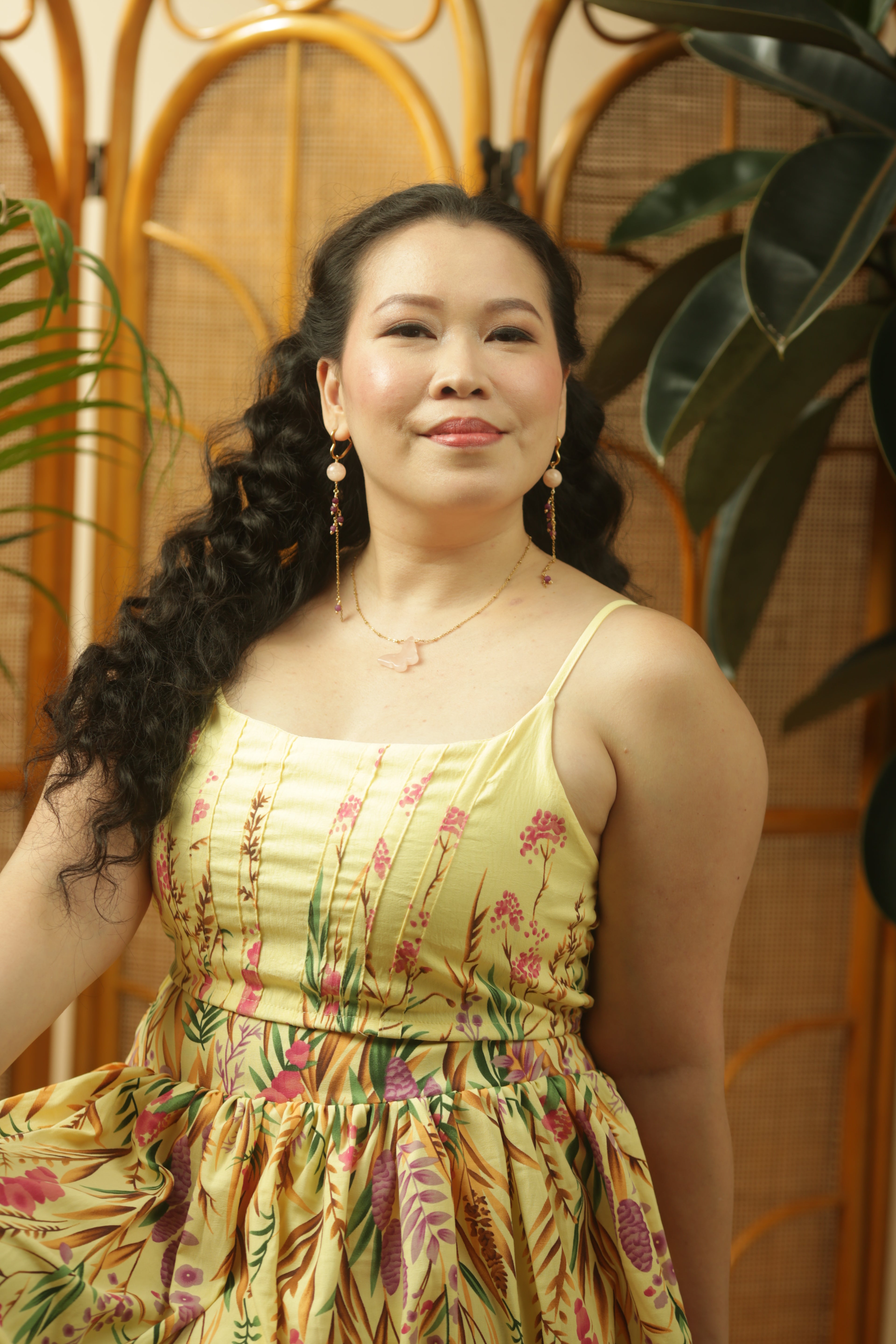 Woman in a floral dress standing in front of a decorative screen with plants.