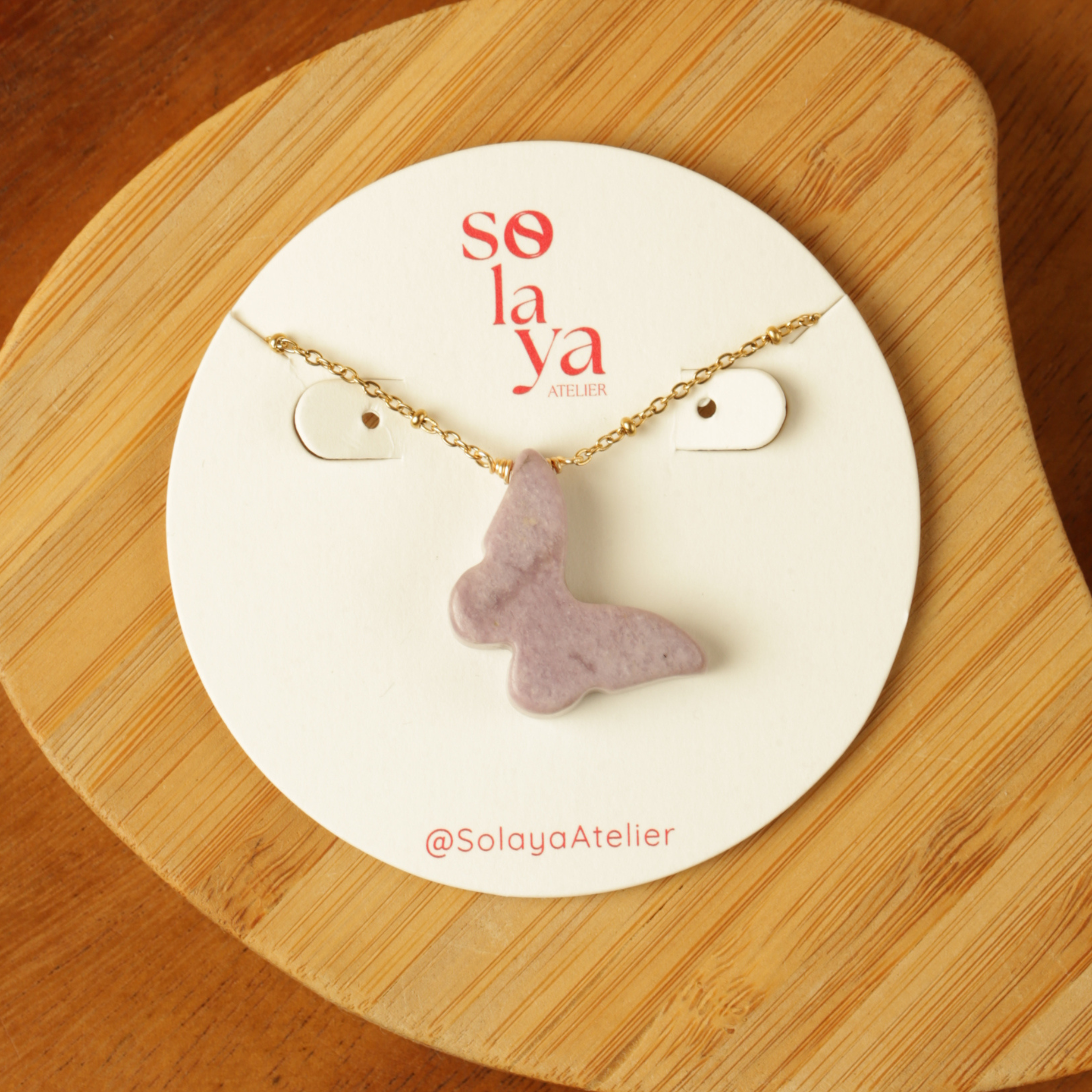 Necklace with a purple pendant on a 'so la ya' branded card on a wooden surface