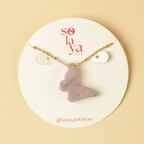 Necklace with a purple pendant on a Solaya Atelier display card against a beige background