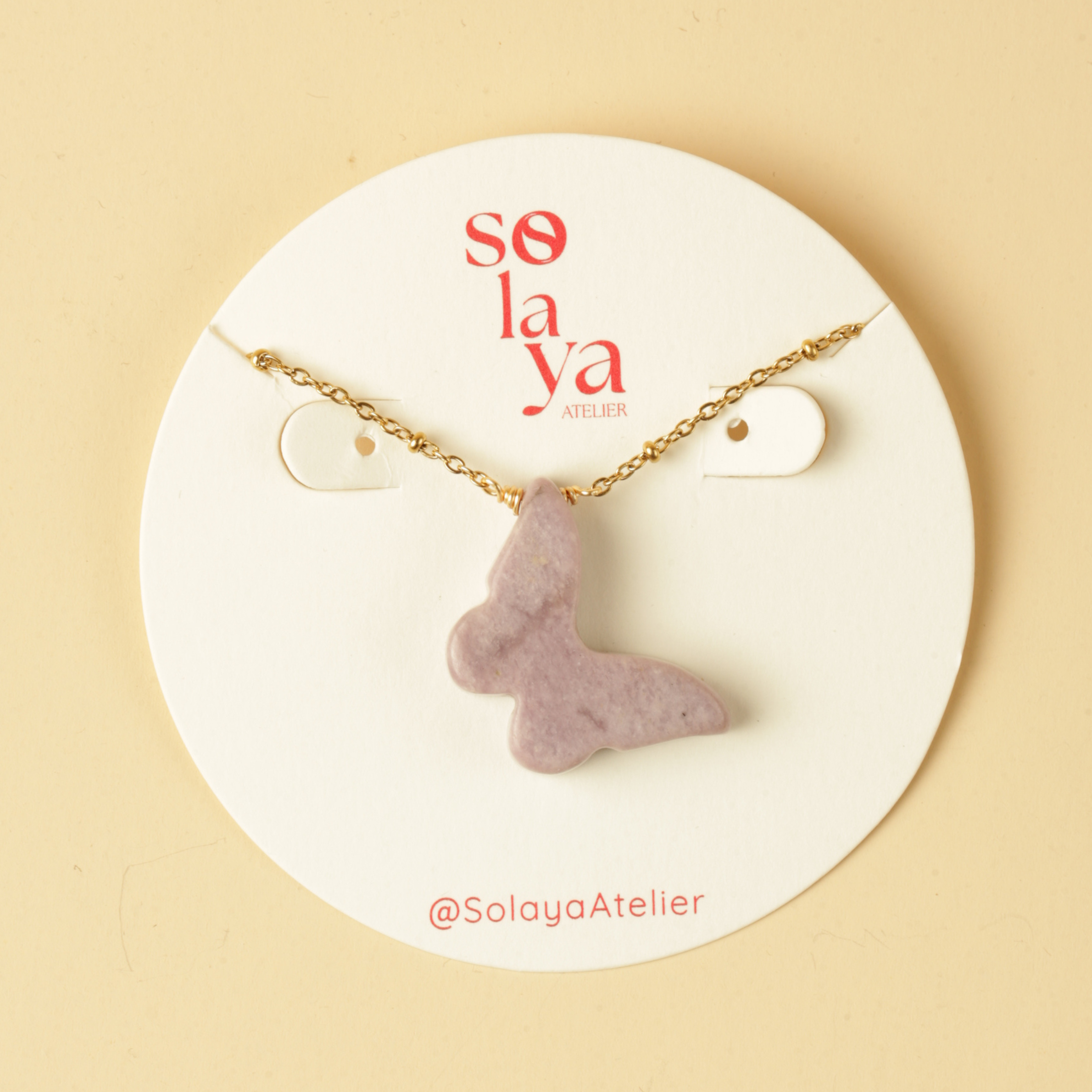 Necklace with a purple pendant on a Solaya Atelier display card against a beige background