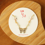 Butterfly necklace on a Solaya Atelier branded card on a wooden surface