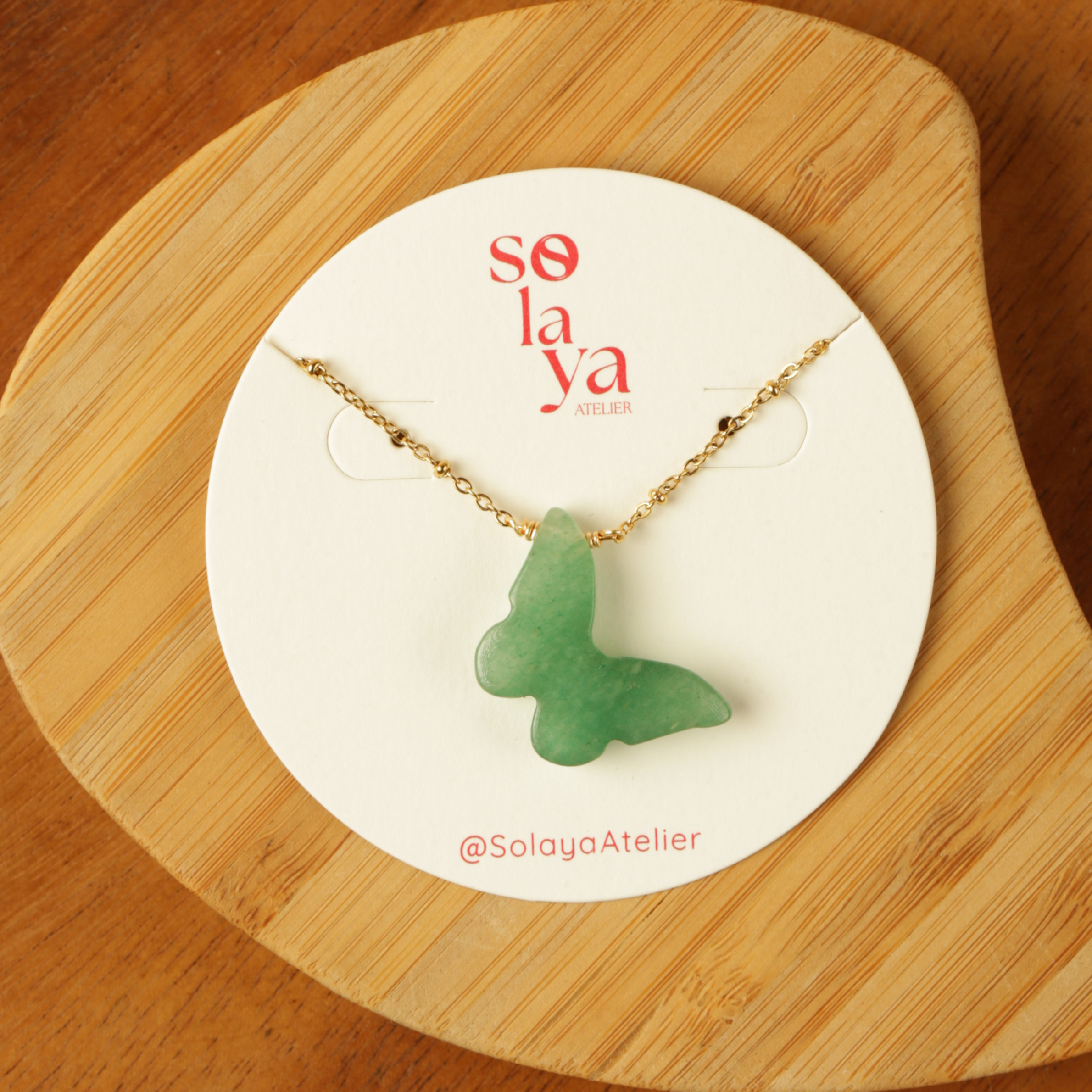 Green butterfly necklace on a Solaya Atelier card with a wooden background
