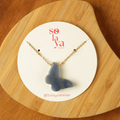 Blue butterfly pendant necklace on a Solaya Atelier card with wooden background