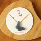 Blue butterfly pendant necklace on a Solaya Atelier card with wooden background