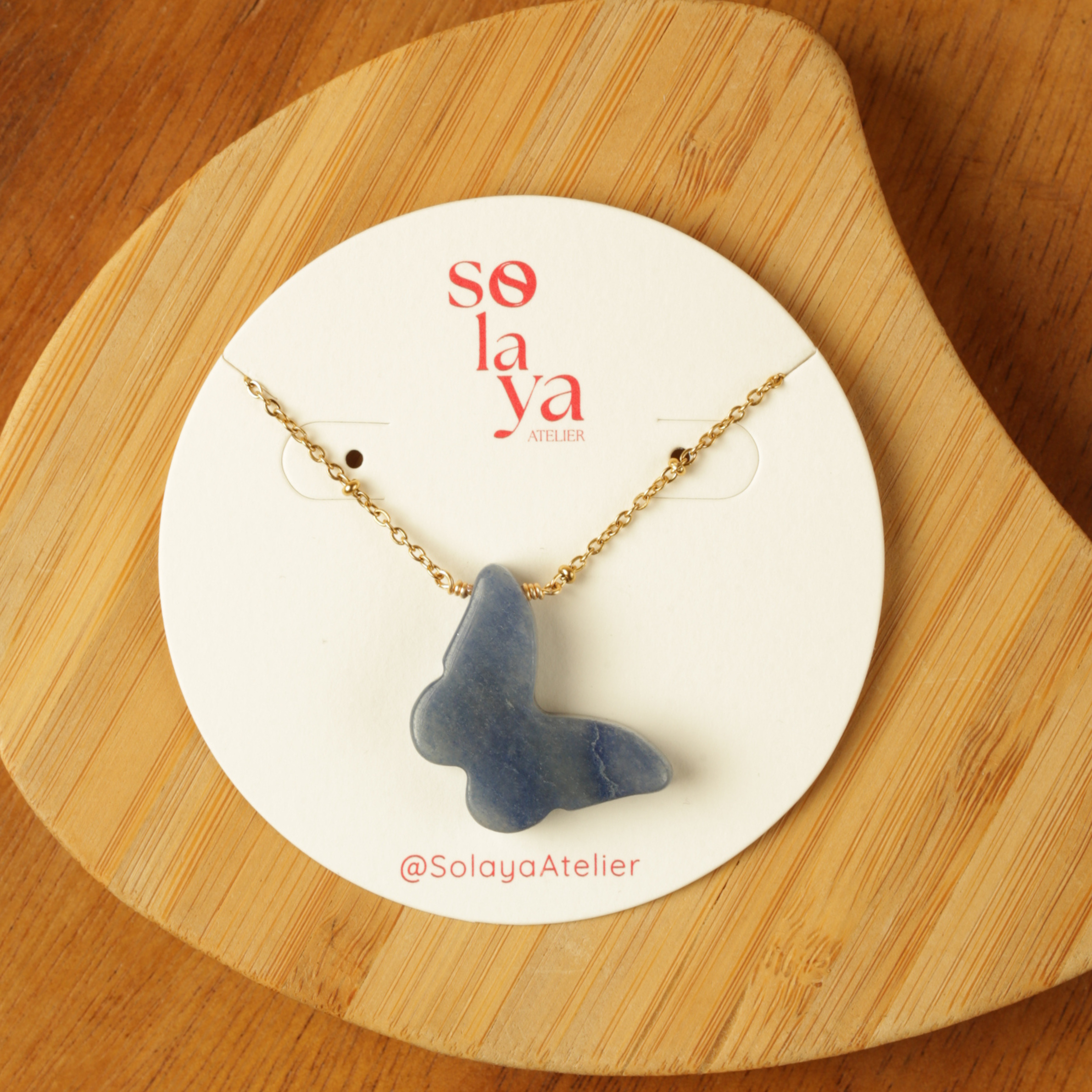 Blue butterfly pendant necklace on a Solaya Atelier card with wooden background