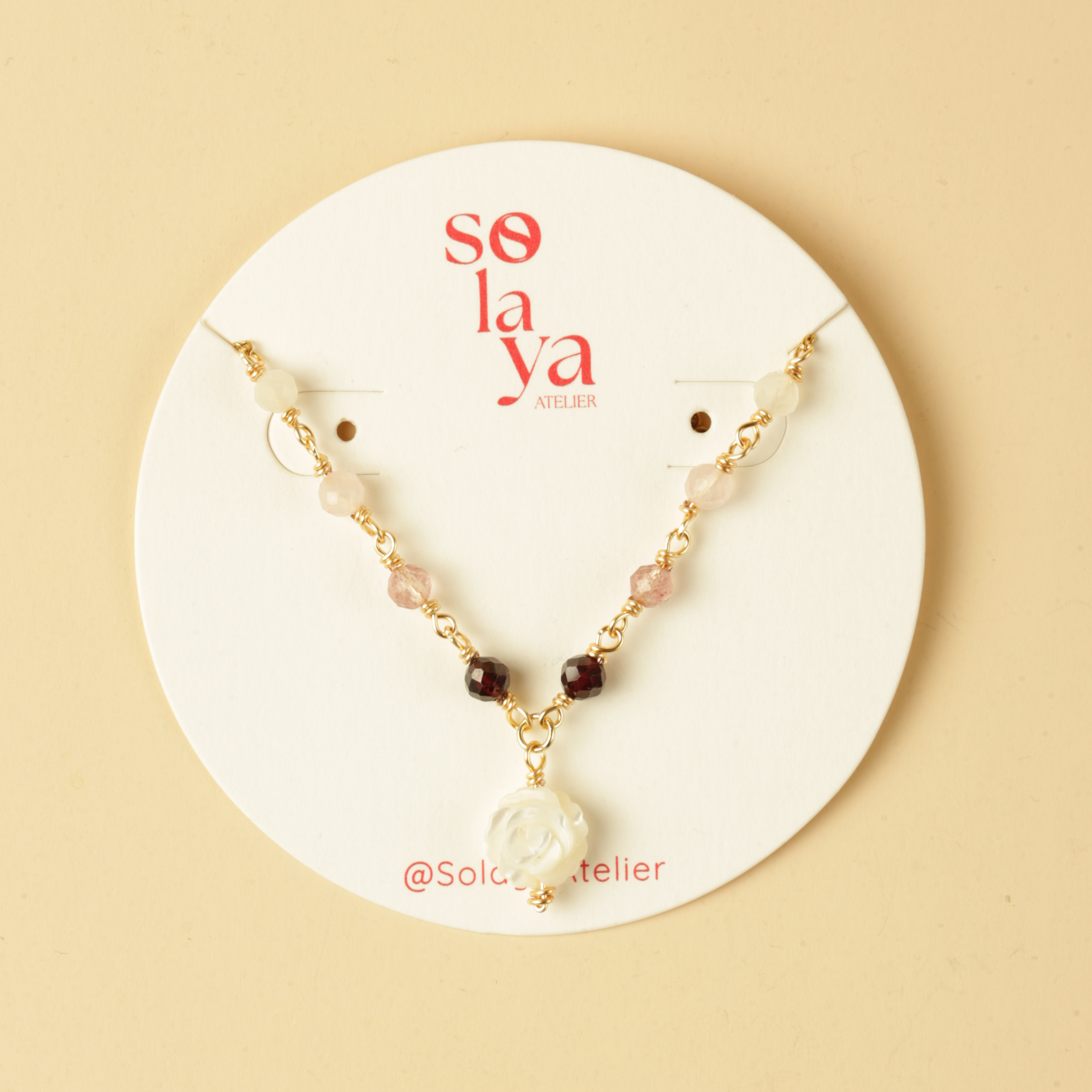 Necklace with floral pendant on a 'so la ya atelier' branded card against a beige background