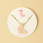 Necklace with a pink cat-shaped pendant on a Solaya Atelier branded card against a beige background