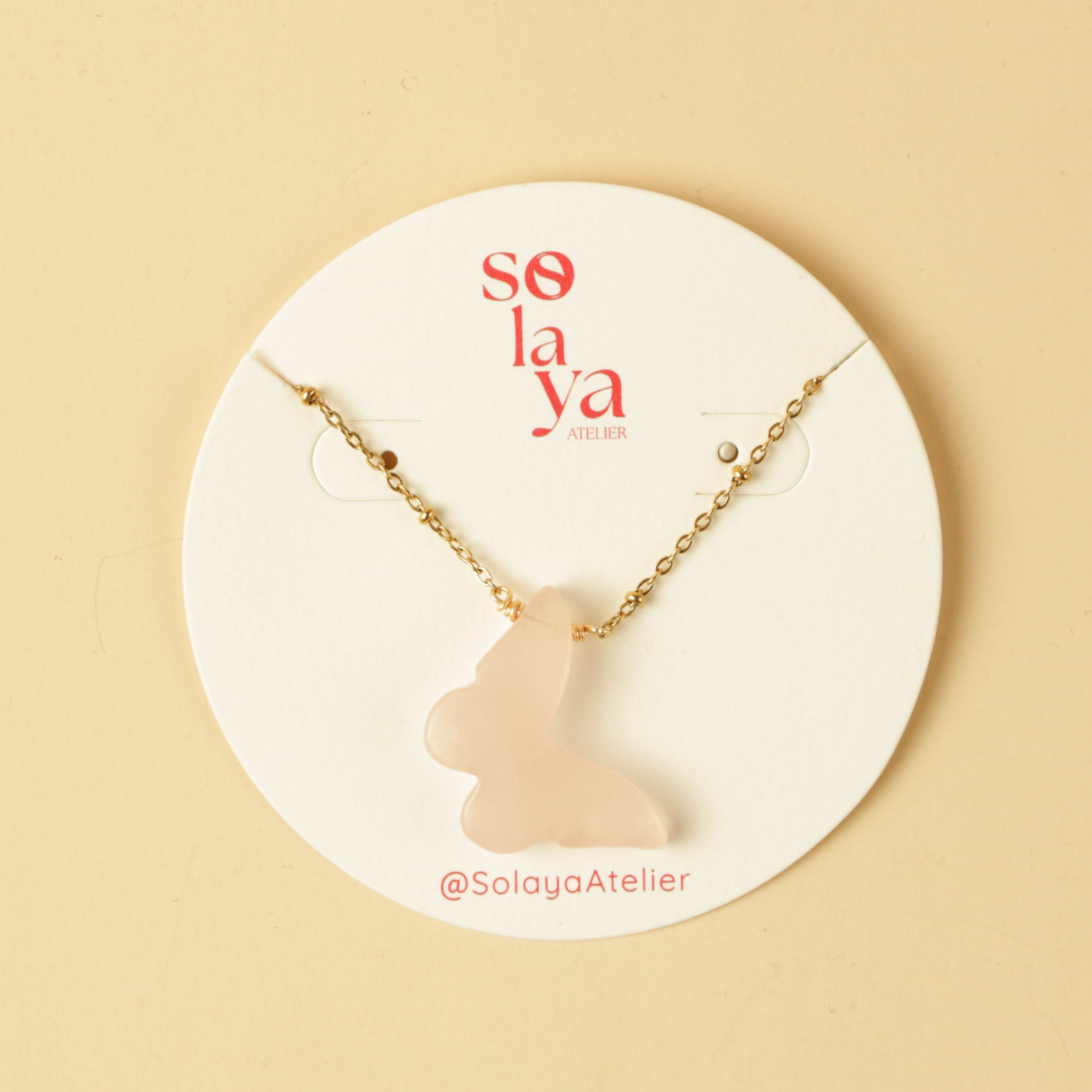 Necklace with a pink cat-shaped pendant on a Solaya Atelier branded card against a beige background